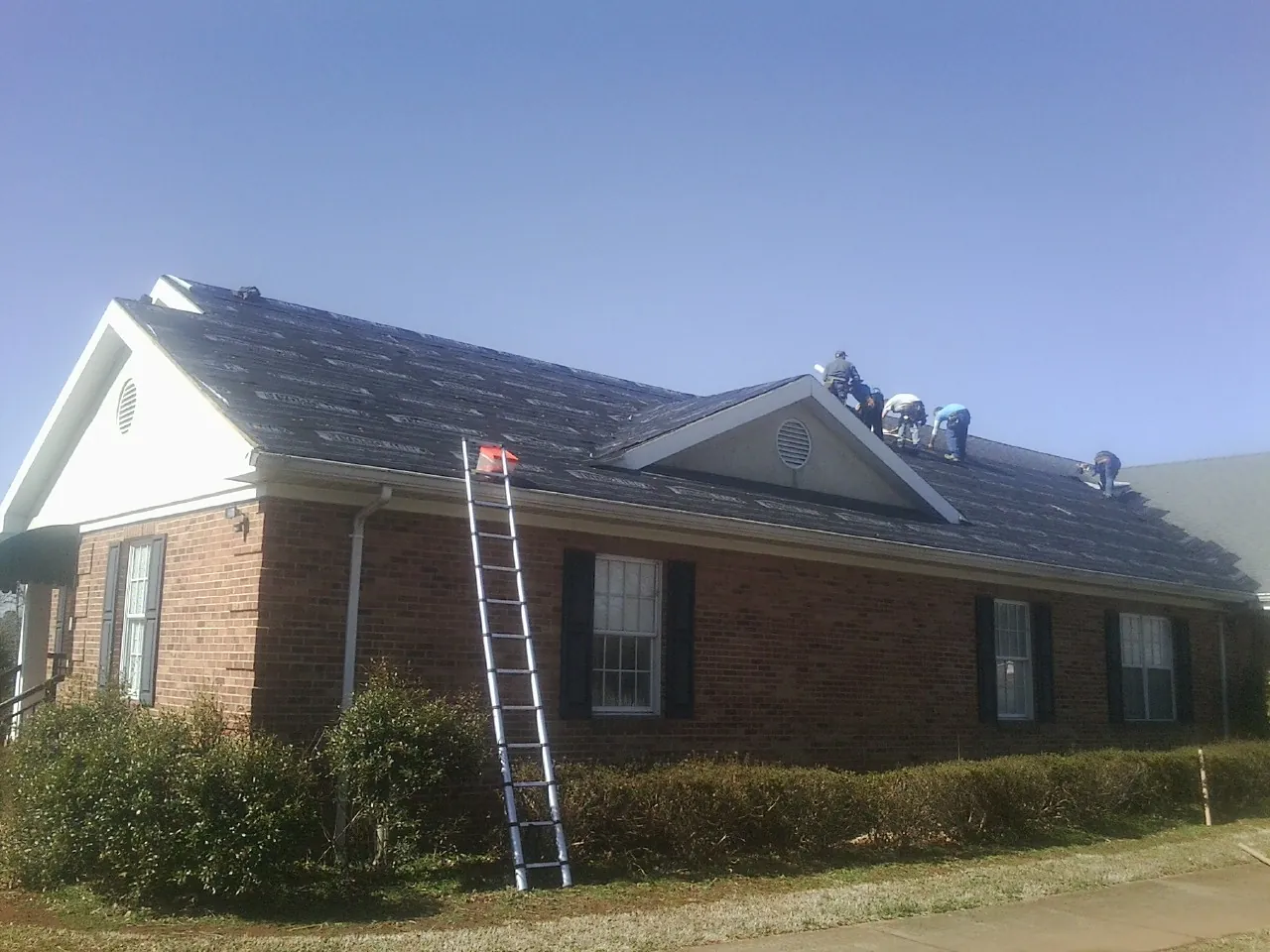 Crew tearing shingles off a brick ranch roof with a ladder set — Emergency Roof Repair work by our crew in Vaughan