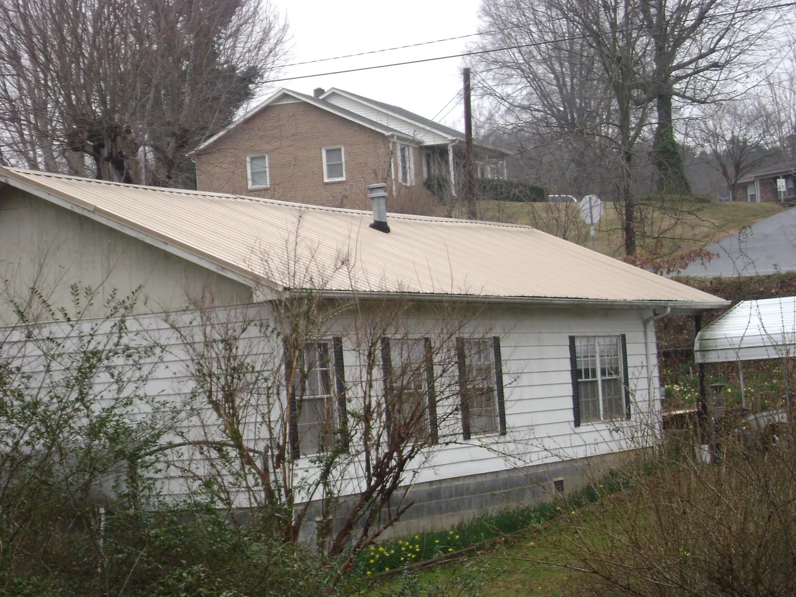 Tan metal roof on a white sided house set into a hillside — Commercial Roofing by Roofing Brothers in Vaughan